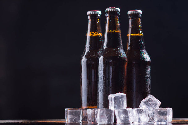 Szklane butelki piwa ze szkłem i lodem na ciemnym tle - Zdjęcie, obraz