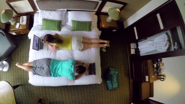 TOP DOWN: Male and female digital nomads working on computers from their hotel room while lying on the comfortable king size bed. Young tourist couple surfing the internet in their holiday suite. - Footage, Video