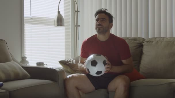 Man in couch holding soccer ball and going through plays in his head - Video
