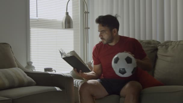 Man holding soccer ball while learning soccer moves from a book - Footage, Video