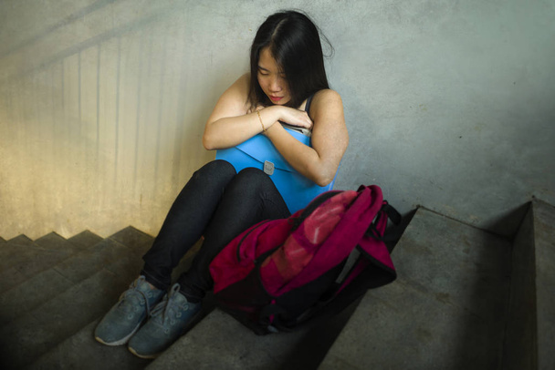 Dramatic portrait of Asian female college student bullied. Young depressed and sad Chinese girl sitting lonely on campus staircase suffering bullying and harassment - Foto, afbeelding