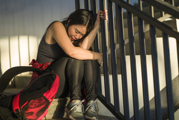 Δραματικό πορτρέτο της ασιατικής γυναικείας φοιτητικής σχολής που εκφοβίζουν. Νεαρή θλιμμένη και λυπημένη Κινέζα που κάθεται μόνη στη σκάλα του Πανεπιστημίου και υποφέρει από εκφοβισμό και παρενόχληση - Φωτογραφία, εικόνα