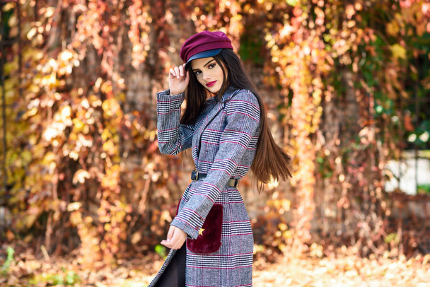 若いです美しい女の子身に着けている冬のコートとキャップで秋の葉の背景. - 写真・画像