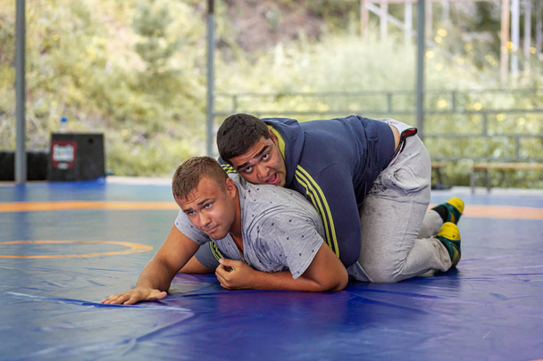 Altai, Rússia 16 de agosto de 2019: Dois homens fortes de roupas esportivas estão lutando em um tapete azul de luta livre no ginásio. Treinamento aberto e acampamentos esportivos de verão
  - Foto, Imagem