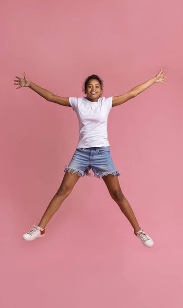 Alegre chica negra saltando con las manos arriba, fondo rosa estudio
 - Foto, imagen