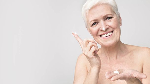 Senhora sênior alegre aplicando loção anti-envelhecimento em seu rosto
 - Foto, Imagem