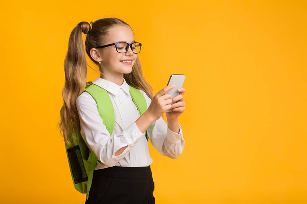 Sarı Arka Planda Cep Telefonu Kullanan Sevimli Gülümseyen Okul Kız - Fotoğraf, Görsel