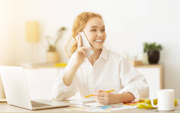 Щаслива швачка розмовляє по телефону, обговорюючи вбрання з клієнтом
 - Фото, зображення