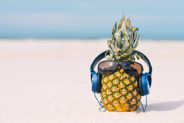 Ananas avec lunettes de soleil et écouteurs sur sable contre l'eau de mer turquoise. Concept de vacances tropicales d'été. Journée ensoleillée d'été sur la plage de l'île tropicale
 - Photo, image