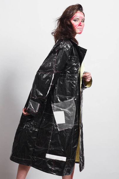 Model in a black raincoat made of cellophane and in creative make-up - Zdjęcie, obraz