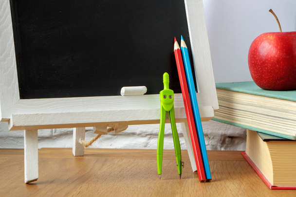 Schulbedarf, Miniatur-Kreidetafel, ein Stapel Bücher und ein Apfel auf dem Tisch, weicher Fokus - Foto, Bild