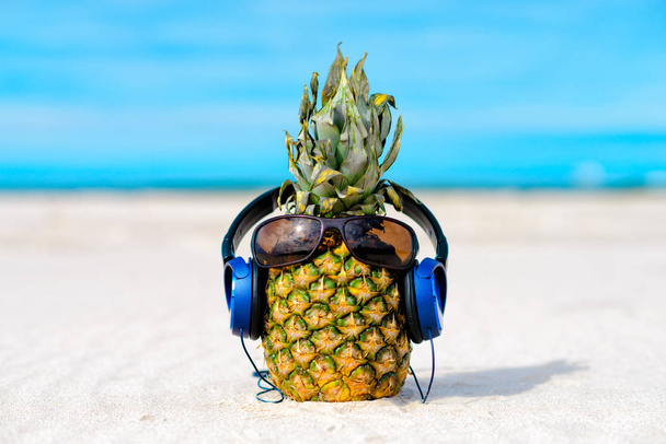 Ananas con occhiali da sole e cuffie sulla spiaggia sabbiosa
 - Foto, immagini