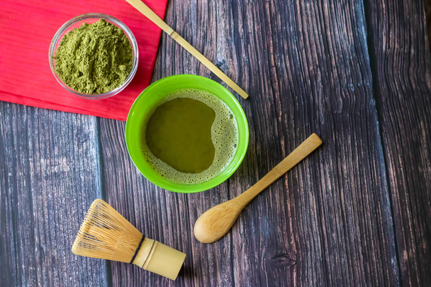 Match green tea in a bowl on a wooden surface with a red napkin. Top view, contains antioxidants, detox. Horizontal orientation - Fotografie, Obrázek