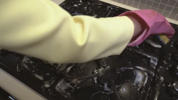 Kobiety ręka w gumowej rękawiczce myje brudną kuchenkę gazową z gąbką. - Materiał filmowy, wideo