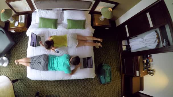 TOP DOWN : Une jeune femme caucasienne tend un téléphone portable à son petit ami tout en travaillant dans le confort de leur chambre d'hôtel. Couple touristique travaillant sur leurs ordinateurs portables pendant leurs vacances amusantes au Vietnam
. - Séquence, vidéo