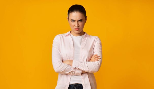 Vihainen nuori nainen Frowning Crossing kädet keltaisella taustalla
 - Valokuva, kuva