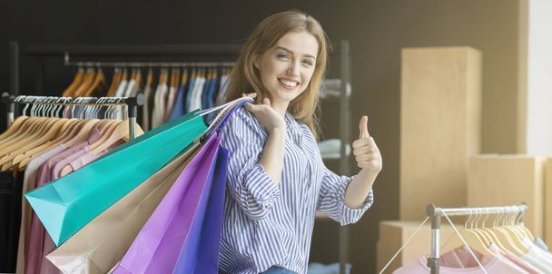 Sonriente chica joven llevando bolsas de compras en el hombro, mostrando el pulgar hacia arriba
 - Foto, imagen