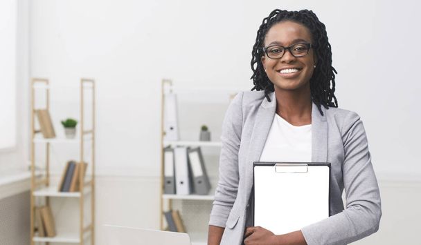 Afroameričanka s hospodářstvím ve složce s úsměvem na fotoaparátu v kanceláři - Fotografie, Obrázek