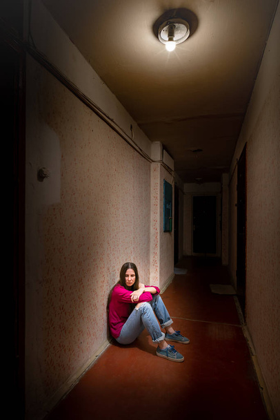Trieste en wanhopige vrouw zit in een donkere gang - Foto, afbeelding