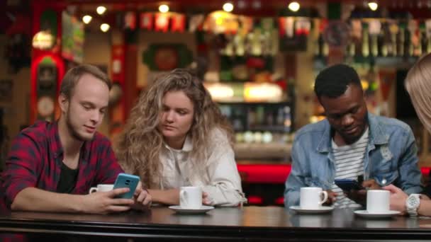 Dwóch mężczyzn i dwie kobiety Multi-etniczne pary siedzieć w kawiarni i spojrzeć na ekrany smartfonów i omówić - Materiał filmowy, wideo