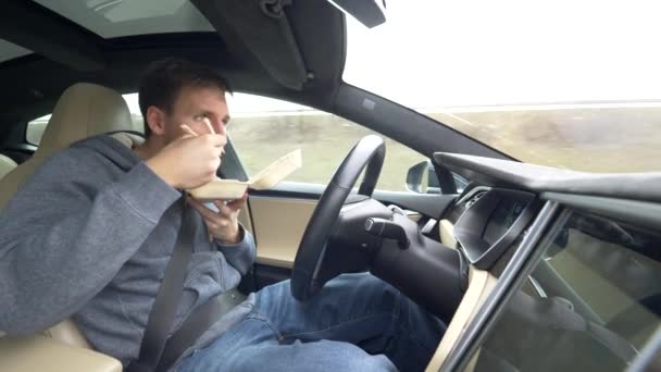 Close-up: roekeloze jonge man die Chinees eet, neemt eten met eetstokjes mee tijdens het rijden in zijn high tech-auto. Mannelijke chauffeur eten tijdens het rijden terug naar huis van het werk. Man rijden in autonoom voertuig. - Video