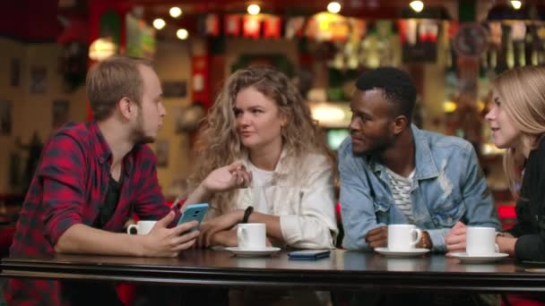 Cheerful company of friends at a bar drinking coffee laughing and discussing while looking at the smartphone screen - Footage, Video