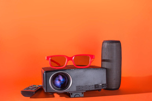 Heimkino-Set: Projektor mit Fernbedienung, 3D-Brille, drahtloser Lautsprecher. orange isolierter Hintergrund - Foto, Bild