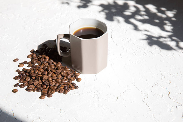 Light brown coffee mug and a scattering of coffee beans on a white textured background. - Foto, Bild