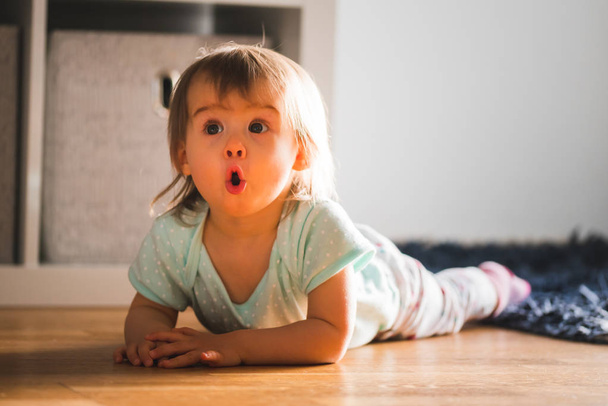 Adorable baby girl lying down on the carpet with funny expression - Fotografie, Obrázek