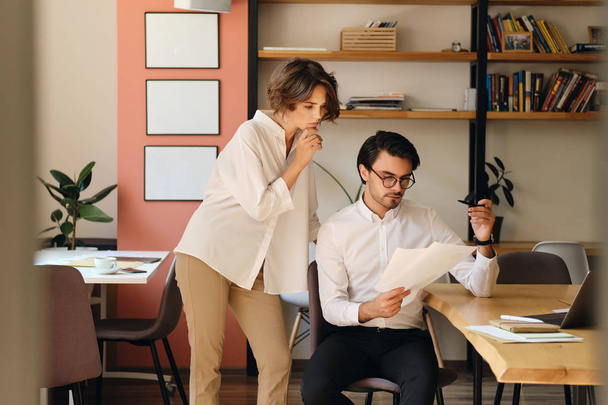 Двое молодых деловых коллег задумчиво работают с бумагами в современном офисе
 - Фото, изображение