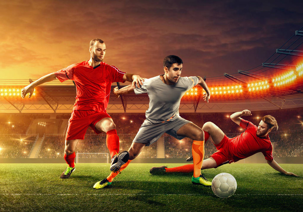 Τρεις ποδοσφαιριστές παλεύουν για μια μπάλα κατά τη διάρκεια του παιχνιδιού σε επαγγελματικό στάδιο με ανεμιστήρες - Φωτογραφία, εικόνα