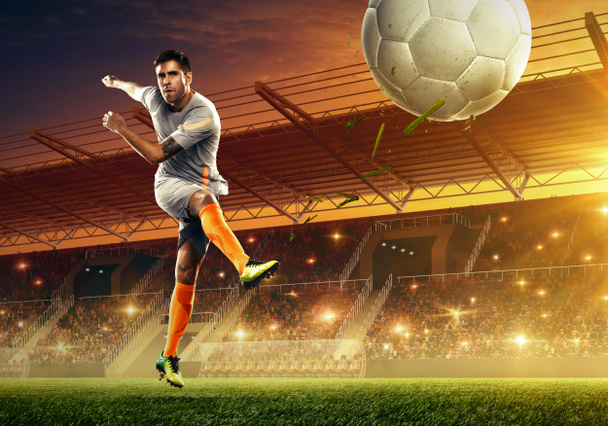 Profesjonalny piłkarz w akcji na oświetlonym stadionie piłkarskim z fanami  - Zdjęcie, obraz
