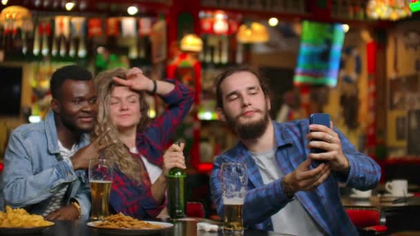 groep vrienden man en twee meisjes nemen selfie in een bar lachen en glimlachen. Tijd doorbrengen met dumbfounds in een bar. - Video