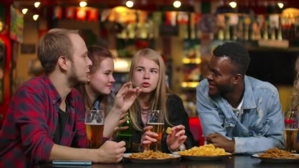 A large cheerful company of young people in the bar chatting, discussing the semester, the latest rumors, laughing and drinking beer. Multi-ethnic company - Footage, Video