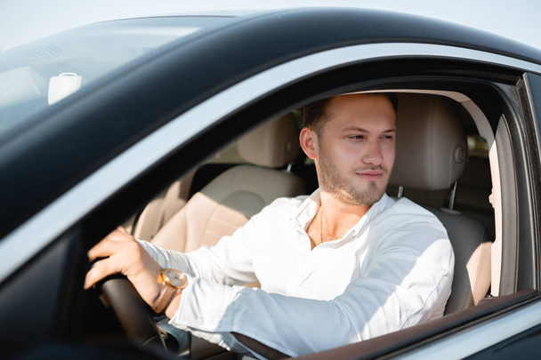 Портрет счастливого водителя в белой рубашке за рулем своей роскошной машины
. - Фото, изображение