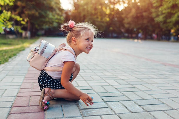 Boldog kislány visel hátizsák és rajz kréta szabadban általános iskolában. Gyerek szórakozik után osztályok - Fotó, kép