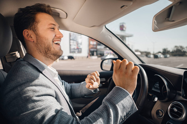 Onnellinen kuljettaja puvussa tanssii ylellisessä autossaan kuunnellen musiikkia ja nauttien elämästä.
. - Valokuva, kuva