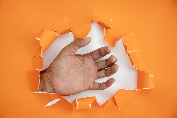 männliche Hand zerrissenes orangefarbenes Papier auf weißem Hintergrund - Foto, Bild