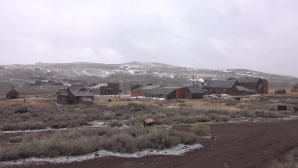 Lichte sneeuwstorm begint ter dekking van de idyllische ghost town in het midden van het ruige landschap. Pittoreske schot van rottende houten weathering een andere koude winter in de prachtige wildernis van Nevada. - Video