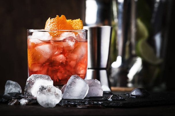 Americano Alcohol cocktail with red vermouth, bitter, soda, orange zest and ice, dark wooden bar counter background, bar tools, selective focus - Фото, зображення