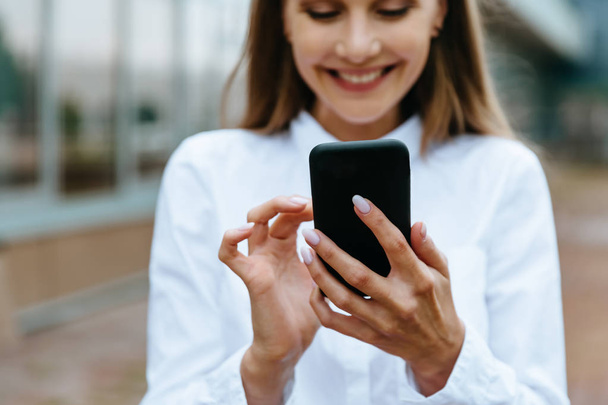 Cropped view of businesswoman using smartphone. Successful female entrepreneur checking email on smartphone. Female texting message. Office building Background. Technology internet and happy people - Fotoğraf, Görsel