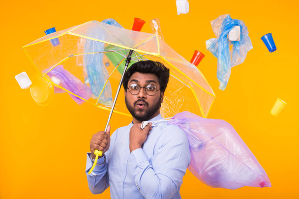 環境汚染、プラスチックリサイクル問題、廃棄物処理の概念 -黄色の背景にゴミ袋を持つインド人男性を驚かせた. - 写真・画像