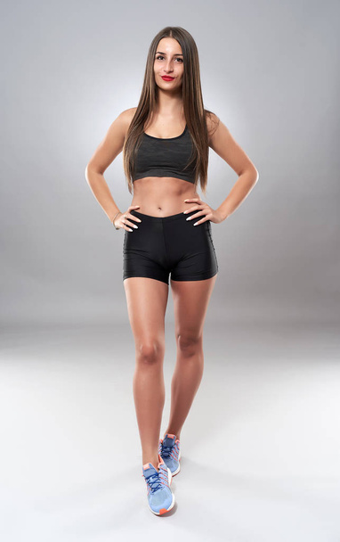 Young athletic woman posing as fitness model on gray background - Photo, image