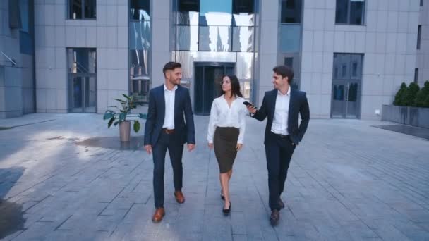 Successful Business People Discuss Business and walk in Central Business District. Two Young Men and one Woman in Suit Communicate and walk near the Office Building of Business Center. - Footage, Video