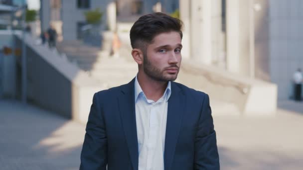 Portrait of successful young businessman in suit standing in city near business center enjoying professional urban lifestyle. Handsome male employee looking at camera. - Footage, Video