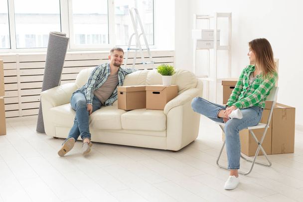 肯定的な陽気なカップルは、自分の持ち物とリビングルームに座って彼らの新しいアパートを移動することに喜び。若い家族のための住宅温暖化と住宅ローンの概念. - 写真・画像