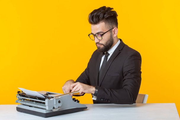 Άραβας επιχειρηματίας ή διευθυντής σε επίσημο κοστούμι δακτυλογραφήσει κείμενο σε μια γραφομηχανή σε κίτρινο φόντο. Έννοια της επιχείρησης και εργασία γραφείου - Φωτογραφία, εικόνα