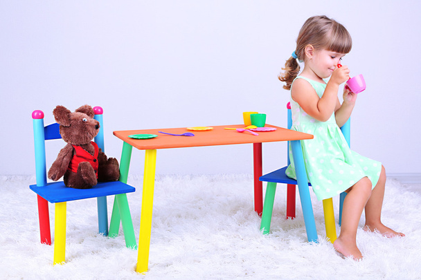 Little cute girl sitting on little chair near table, on gray background - Zdjęcie, obraz