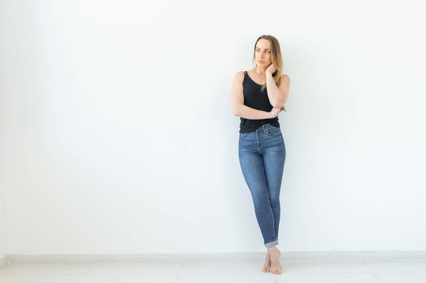 Style, people concept - young woman in jeans and black shirt standing over the white background with copy space - Фото, изображение