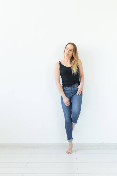 Концепция стиля и людей - молодая женщина в джинсах стоит над белой стеной и выглядит как сексуальная
 - Фото, изображение